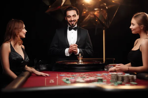 A professional dealer in a tuxedo greeting players at the roulette table, symbolizing the authentic live casino feel at GOOD111.