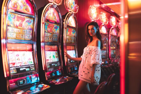 A stylish woman beside vibrant slot machines displaying glowing sevens, showcasing the variety of top slots at GOOD111.